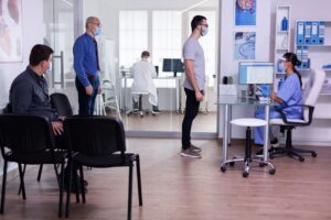 young man checking appointment respecting social distancing hospital waiting room nurse looking computer wearing face mask against covid